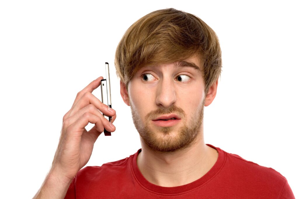 A man with brown hair, wearing a red shirt, holding a phone near his ear