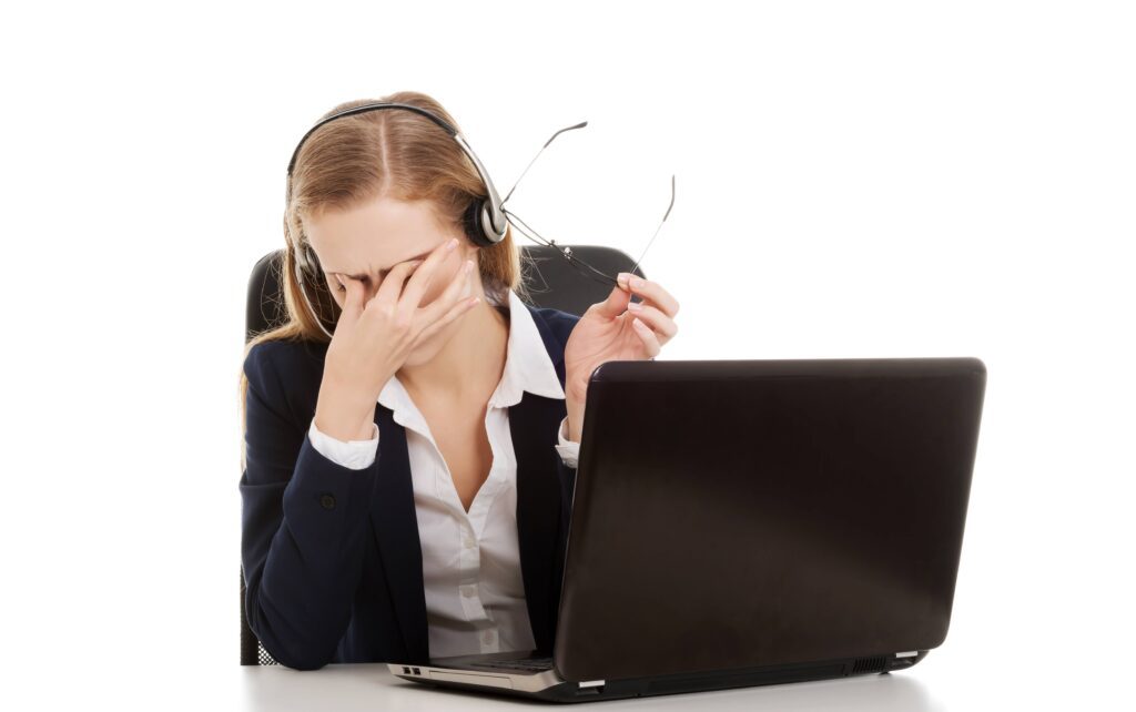 A woman in front of her laptop, touching her eyes while holding her eyeglasses